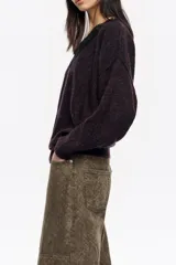 Jersey de punto en mezcla de mohair y lana, color negro con efecto jaspeado. Presenta un escote en V decorado con una aplicación de encaje negro y mangas largas con corte holgado.