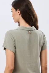 Camisa lisa de lino color beige, de manga corta, con cuello camisero, bolsillo ojal en el pecho y cierre frontal con botones.