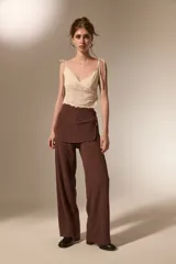 Pantalon de corte recto y tiro alto, confeccionado en tela texturizada color marrón, con detalle de falda superpuesta en la cintura.