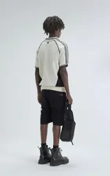 Chomba tejida de punto cerrado color off-white, con cuello polo y ribetes negros. Presenta un diseño deportivo con paneles laterales negros, número "90" y texto "Ravers" bordado en el frente.