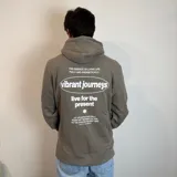 Canguro color caqui con capucha y cordón ajustable. Estampado en la espalda con la frase "The essence of living life fully and energetically", el logo "vibrant journeys", la frase "live for the present" y una cita de Santa Barbara.