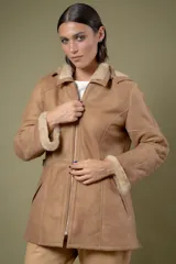 Campera de babylamb color beige con interior de piel sintética al tono. Presenta cierre frontal, capucha desmontable, bolsillos laterales, presillas ajustables en la cintura y cierres en los laterales del ruedo.