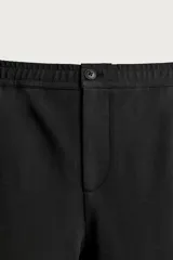 Pantalón negro confeccionado en mezcla de algodón, con cintura elástica, bolsillos frontales y cierre con cremallera y botón.