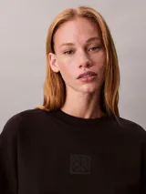 Buzo de felpa Calvin Klein de color negro, corte regular y cuello redondo, con el nuevo emblema con logo texturizado en el pecho y puños, cuello y bajo de canalé.