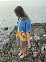 Poncho corto azul con franja horizontal amarilla y bolsillo estampado con motivos florales.