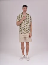 Camisa de manga corta con estampado de hojas color verde sobre fondo beige, cuello solapa y bolsillo en el pecho.