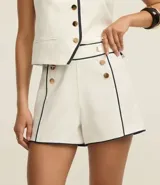 Short sastre de cintura alta confeccionado en crepé color blanco, con botones delanteros metalizados, cierre lateral por cremallera, bolsillos falsos atrás y bies contrastante en color negro.