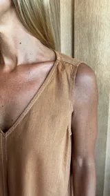 Vestido largo de denim azul, con escote en V, sin mangas, corte holgado, bolsillos laterales y aberturas en los costados de la falda.