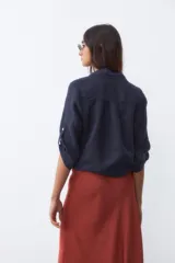Camisa de lino color azul marino, con cuello clásico, cierre frontal de botones y mangas tres cuartos con trabilla. Presenta un diseño con nudo en la parte inferior delantera.