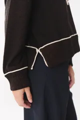 Buzo de tejido de punto en color azul marino, con cuello alto y cierre frontal parcial. Presenta un diseño con franjas en color marrón y detalles de líneas en rojo en el pecho, hombros y ruedo. Tiene corte holgado y mangas largas con puños acanalados.