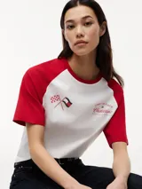 Remera de cuello redondo con diseño de mangas raglán en color rojo y cuerpo en color blanco. Presenta un estampado gráfico en el pecho con banderas de carreras y el logo de la colaboración Tommy Hilfiger x Cadillac Formula 1 Team.