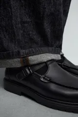 Zapato tipo Mary Jane color negro, con cierre mediante hebilla lateral, parte superior fabricada en piel, detalle de bordón en el empeine, horma redonda y suela con volumen.