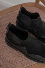 Botas tipo chelsea de caña baja, confeccionadas en una combinación de cuero gamuzado y cuero texturizado en tono marrón oscuro. Presentan una suela track de plataforma gruesa y elásticos laterales negros.