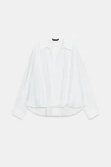 Camisa de lino color blanco, con cuello solapa, escote en V y mangas largas con puños abotonados. Presenta un diseño holgado con bajo asimétrico y pliegues en la parte delantera.