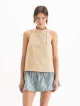 Top Lucille de silueta evasé, calce holgado y corte cropped, confeccionado en poplín Milano de algodón Pima. Cuenta con escote halter de sisa profunda, bretel regulable con ojalillos de níquel que envuelve el cuello, pinzas de entalle y espalda abierta.