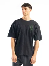 Remera de corte oversized color negro con efecto lavado, cuello redondo y manga corta. Presenta un pequeño estampado gráfico en color verde en el lado izquierdo del pecho.