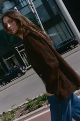 Blazer de piel 100% color marrón oscuro, con cuello solapa, manga larga con hombreras y bolsillos delanteros con solapa. Presenta pespuntes decorativos en contraste y cierre frontal con un botón.