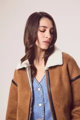 Campera marrón de gamuza sintética con cuello, puños y ruedo de piel sintética blanca. Presenta cierre frontal con cremallera, bolsillos laterales y detalles en cuero sintético negro.
