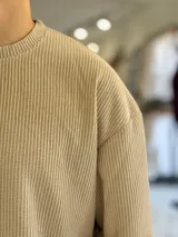 Buzo oversize de tejido waffle en color beige, con cuello redondo y manga larga, con pequeña etiqueta de marca en el dobladillo inferior.