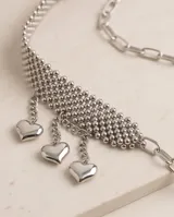 Cinto metálico plateado compuesto por una banda de malla de esferas y una extensión de cadena ajustable con dijes colgantes en forma de corazón.