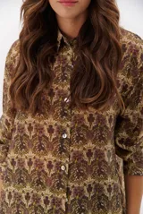 Camisa de manga larga con estampado de tapiz en tonos marrones, verdes y beige. Tiene cuello clásico y cierre frontal con botones.