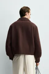 Cazadora boxy fit marrón de corte corto, confeccionada en tejido con mezcla de lana. Presenta cuello camisero, cierre frontal de cremallera metálica, bolsillos de vivo en la cadera y mangas largas.