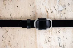 Cinto de cuero negro con hebilla rectangular plateada.