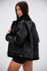 Campera tipo gamulán de corte oversize, confeccionada en cuero sintético con acabado texturizado y forro interior de corderito sintético negro. Presenta cierre frontal, cuello con solapas, detalles de tiras con hebilla en el ruedo y terminaciones en corderito en puños y bordes.