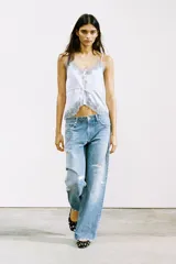 Top satinado color celeste con escote en pico y tirantes finos. Presenta detalles de encaje gris en el escote y el bajo, y una cintura ajustable con lazada.