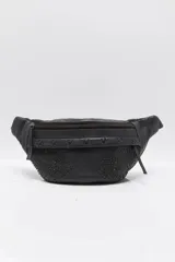 Riñonera de cuero negro con tachas aplicadas en el frente y cierre superior de cremallera.