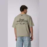 Remera boxy de calce corto y ancho, color verde oliva, con cuello redondo, mangas cortas y estampa frontal minimalista con texto y logo.
