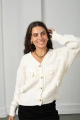 Saco de punto color blanco con cuello en V y cierre frontal de botones. Presenta un diseño con aplicaciones de flores tejidas en relieve y detalles de trenzas verticales.