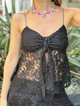 Top de encaje blanco con breteles finos, escote con detalle fruncido y nudo frontal que crea una apertura sutil.