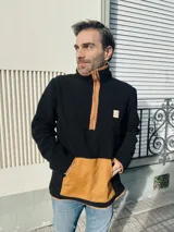 Buzo de hombre de polar negro con cierre parcial color naranja, bolsillo de parche color naranja en la parte inferior y cuello alto.