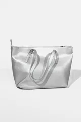 Cartera tipo tote plateada de tela brillante con cierre superior y doble asa corta.
