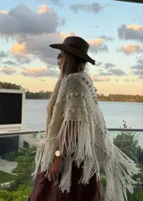 Ruana tejida artesanalmente en color crudo, con diseño triangular, textura de puntos en relieve y terminación con flecos largos en todo el borde.