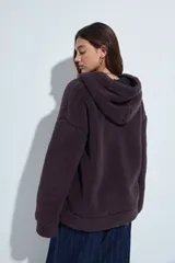 Canguro de corderito con capucha, cierre frontal y bolsillos laterales. Diseño relajado y textura suave.