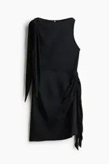 Vestido corto negro con leve brillo, sin mangas, escote bote y detalles de tiras para atar en un hombro y en la cintura con fruncidos laterales.