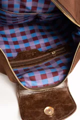 Cartera tipo shopper color marrón, con solapa frontal decorativa en tono más oscuro y tiras con nudos. Incluye herrajes dorados y un charm colgante con cuentas de madera.