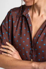 Blusa color crudo con estampado de lunares marrones, cuello camisero, cierre frontal con botones y mangas cortas holgadas.
