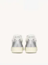 Zapatillas urbanas Autry Open Mid de mujer, inspiradas en el estilo de los años 80. Capellada de cuero plateado y malla blanca, con cordones planos de algodón y suela de goma color crema.