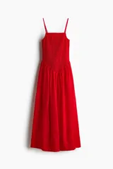 Vestido maxi rojo confeccionado en tejido liviano de algodón, con escote recto, breteles finos y cuerpo fruncido en nido de abeja con costura en V en la cintura, y falda larga con vuelo.