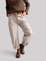 Pantalón de corte recto y tiro medio, color beige, con bolsillos laterales y dobladillo en los tobillos. Incluye un cinturón de cuero sintético con tachas metálicas.