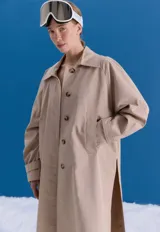 Trench midi color camel, confeccionado en mezcla de algodón y nylon. Presenta cuello clásico, cierre frontal con botones, tajos laterales y bolsillos internos. Es una prenda repelente al agua con diseño versátil y funcional.