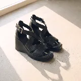 Sandalias de cuero negro con plataforma y taco cuña, diseño de tiras cruzadas en el empeine, puntera cuadrada y tira ajustable con hebilla en el tobillo.