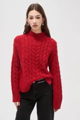 Polera de tejido de punto color crema, con cuello alto y diseño de trenzas verticales. Presenta mangas largas con puños acanalados y un corte holgado.