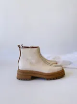 Botas Chelsea de cuero color crudo con elástico lateral, suela track color caramelo y tirador trasero de cuero con textura croco color marrón.