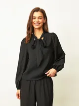 Blusa negra de textura arrugada, con cuello alto y lazo frontal para anudar. Presenta mangas largas abullonadas con puños elásticos y un corte recto.