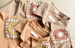 Camisa tostada de manga larga con cuello clásico decorado con apliques de crochet en tonos marrones, blancos y verdes, cierre frontal de botones y diseño holgado.
