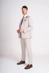 Traje de lino color beige claro, compuesto por saco de dos botones con solapa de muesca, dos bolsillos delanteros con solapa y un bolsillo en el pecho, y pantalón de vestir de corte recto. Incluye camisa blanca, corbata estampada y zapatos marrones.